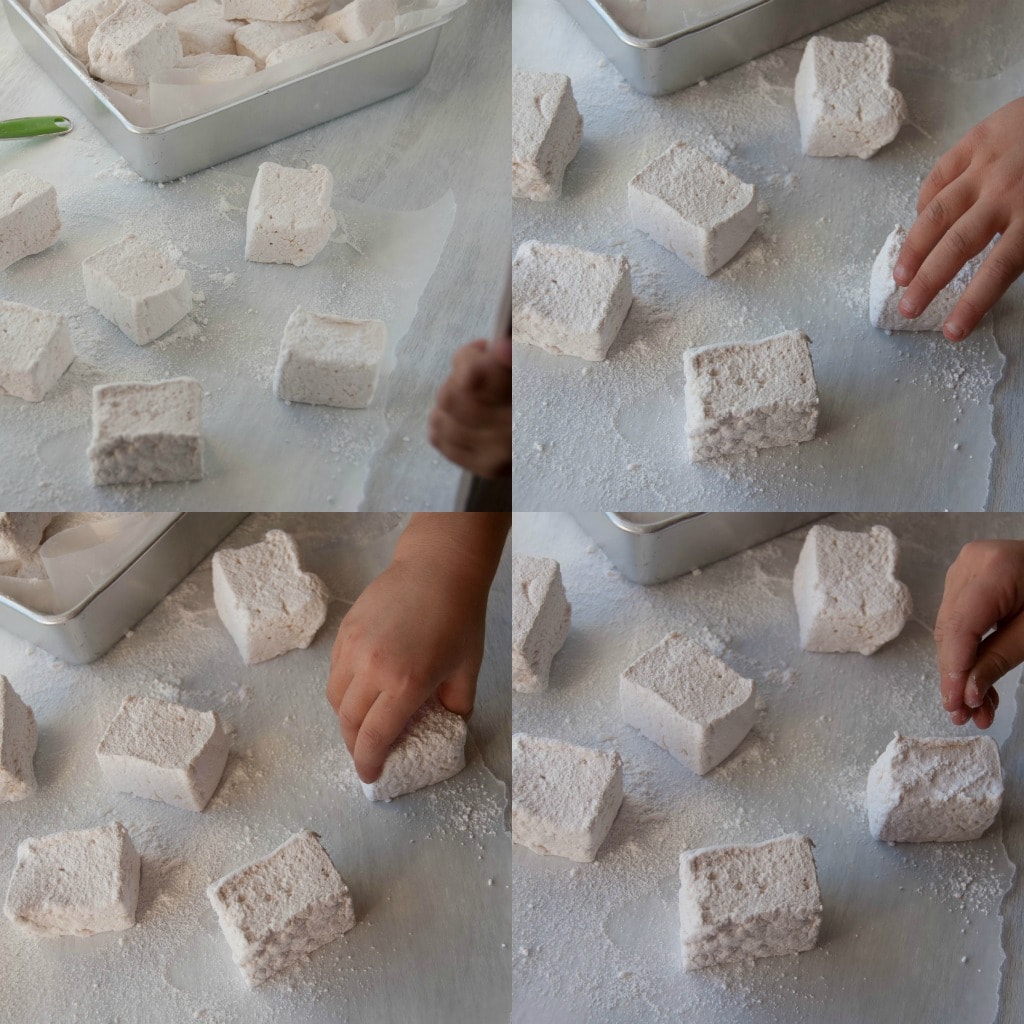 marshmallows being dipped in powdered sugar on parchment paper 