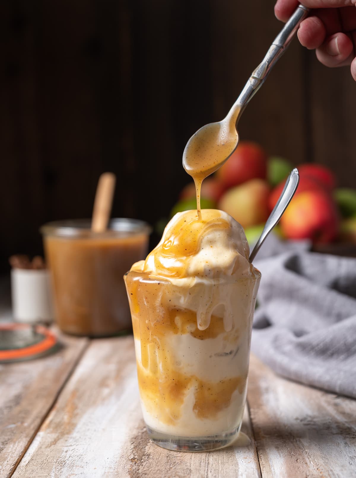 apple cider caramel sauce being poured over a glass cup of ice cream with a spoon