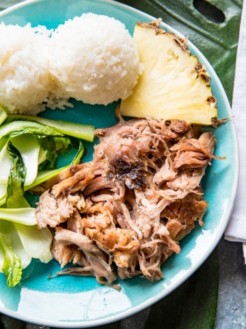 aqua plate with a Hawaiian kalua pork, baby bok choy, pineapple wedge, two scoops of white sticky rice.