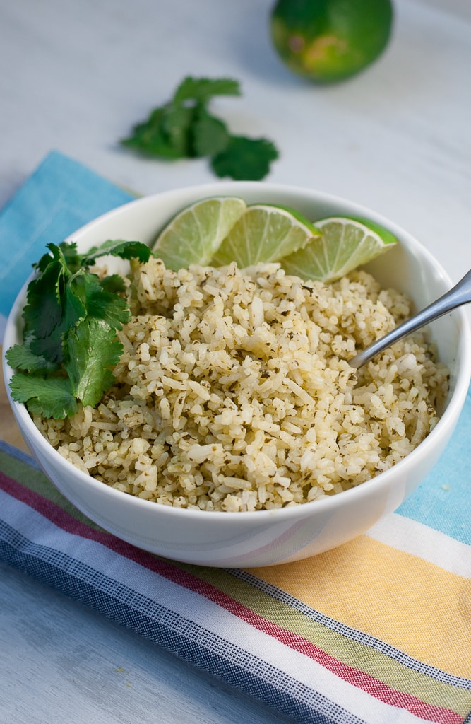 white bowl with green cilantro lime rice limes and fresh cilantro