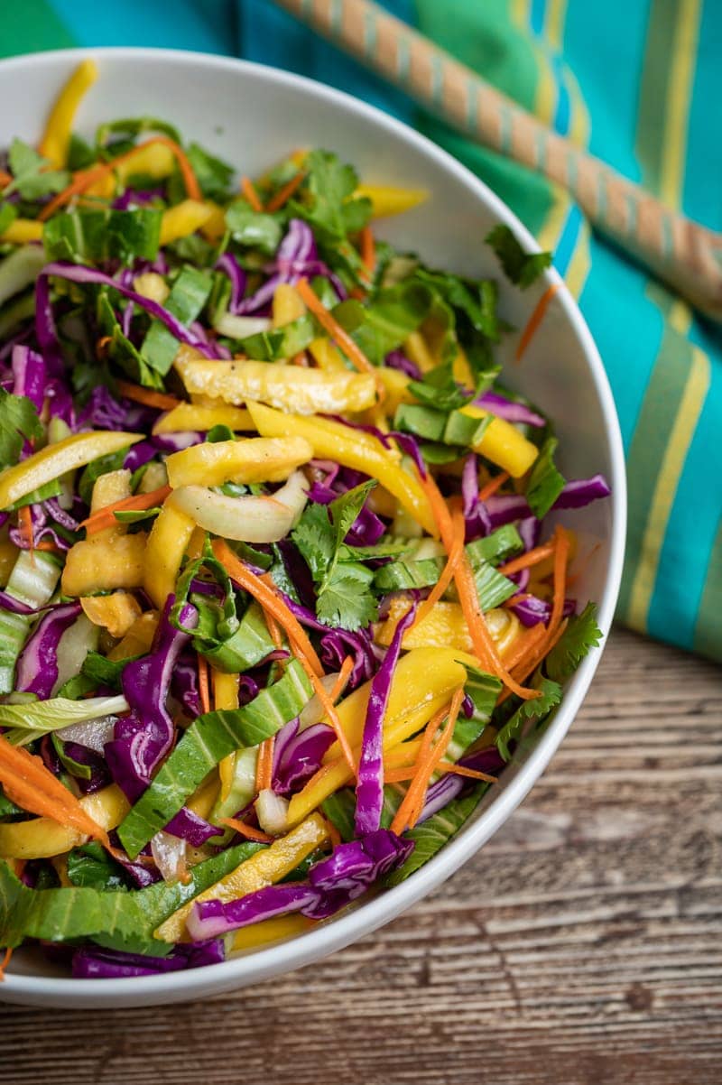 Pineapple Mango Slaw in a white bowl, aqua striped napkin, aqua striped wooden spoon