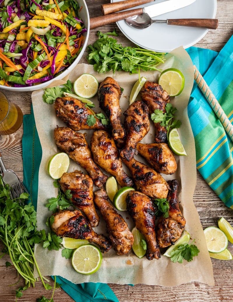 large paper lined tray with seasoned cooked drumsticks, lime slices, and cilantro, bowl of tropical cole slaw