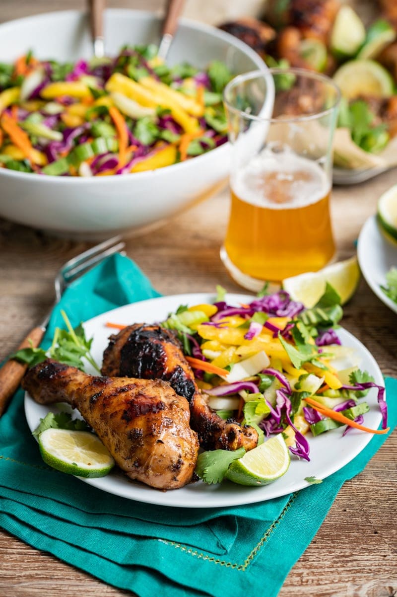 white plate with seasoned grilled chicken drumsticks, large bowl of slaw, glass of beer