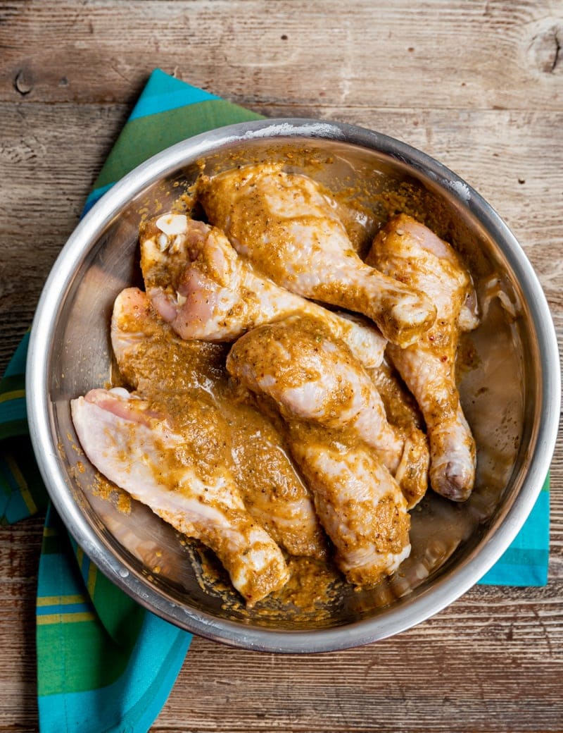 stainless steel bowl with raw chicken drumsticks covered in Jamaican jerk spice seasoning mix