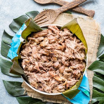 bowl of kalua pork serving spoons monstera leaves