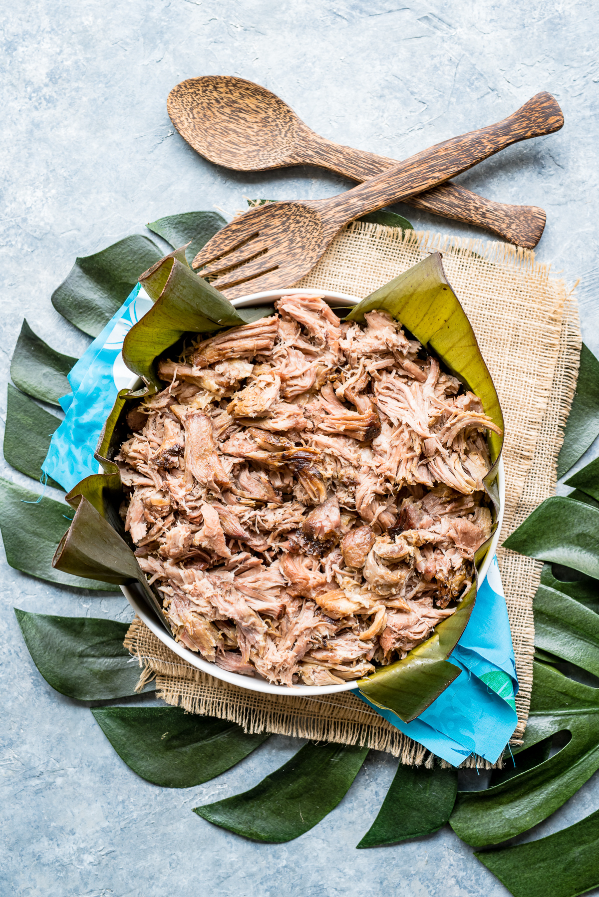 bowl of kalua pork serving spoons monstera leaves