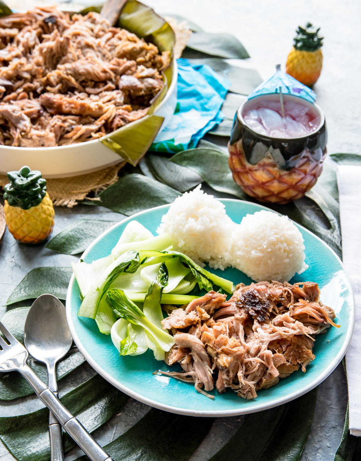 kālua pork on a blue plate with baby bok choy pineapple wedge scoops of white rice