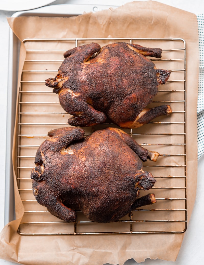 two whole smoked chickens on a wire tray on top of a baking sheet with brown parchment paper