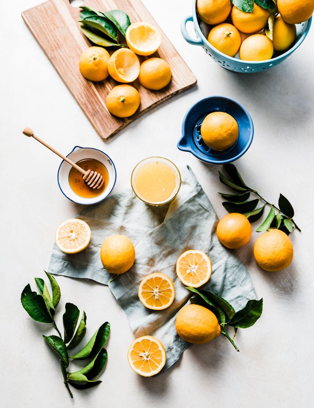 skär och hela citroner, skärbräda med citroner, blå skål fylld med citroner, citronblad, honung i en liten skål med honungspinne, glas citronsaft