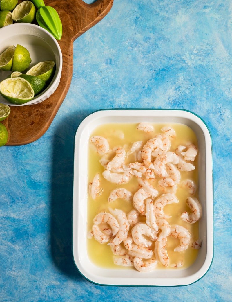 Shrimp Ceviche prep pic, shrimp with lime juice in a shallow pan, limes cut in half on a wood board
