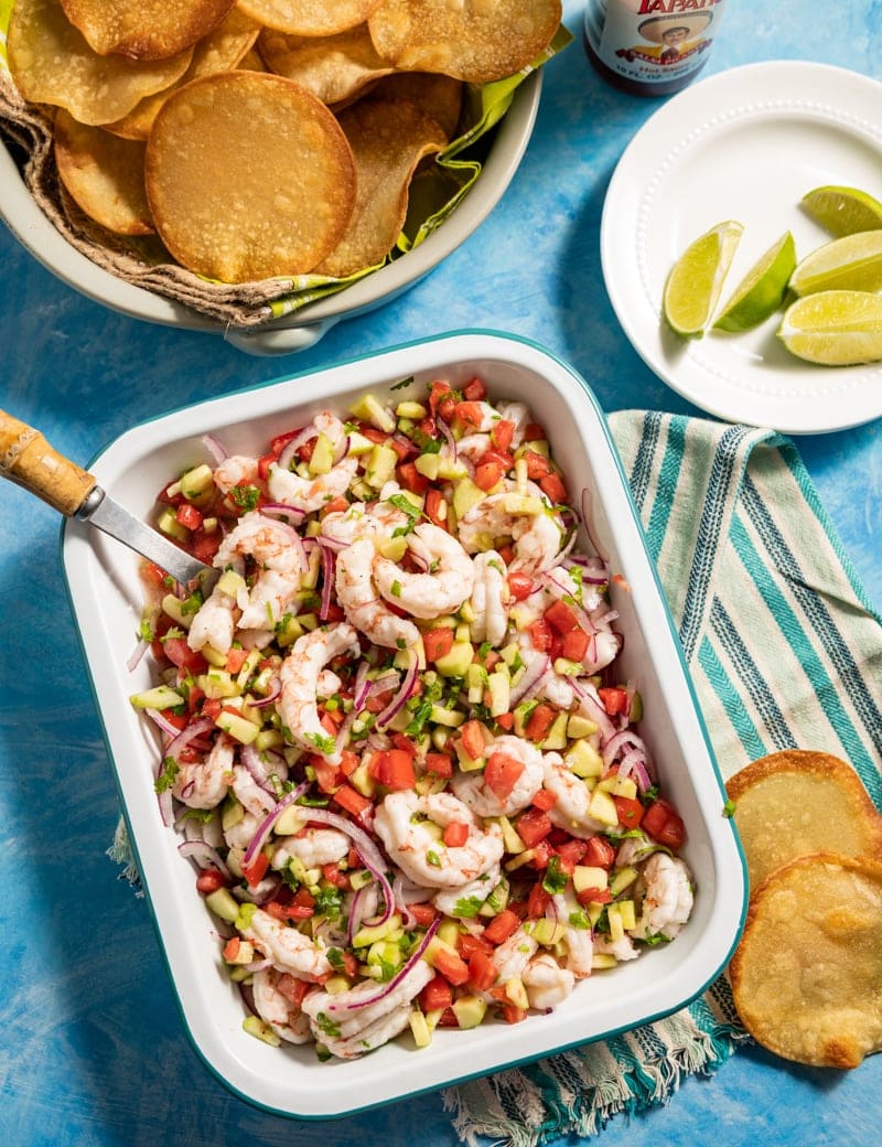 Mini Shrimp Ceviche Tostadas prep pic with mini tostadas in a basket, shrimp ceviche in a pan cut limes on a plate 