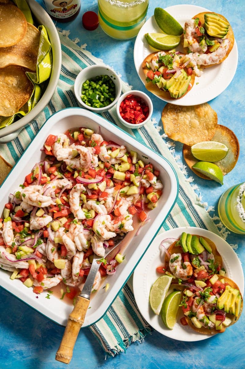 Beautiful food photography of Mini Shrimp Ceviche Tostada recipe with tray of shrimp ceviche, small plates with mini tostadas, margaritas, bowl of chips, bowls of sliced chilies