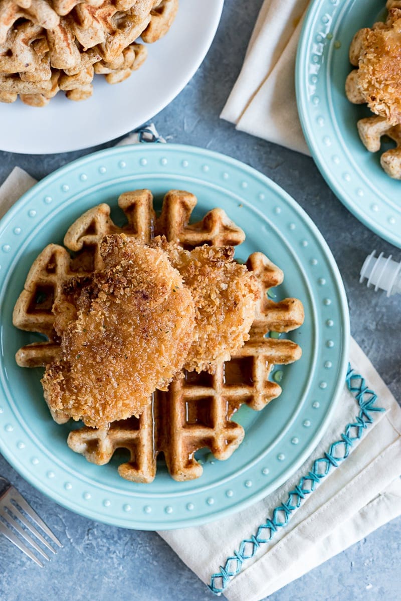 close up of an aqua plate with waffle, chicken tenders, syrup poured over the plate