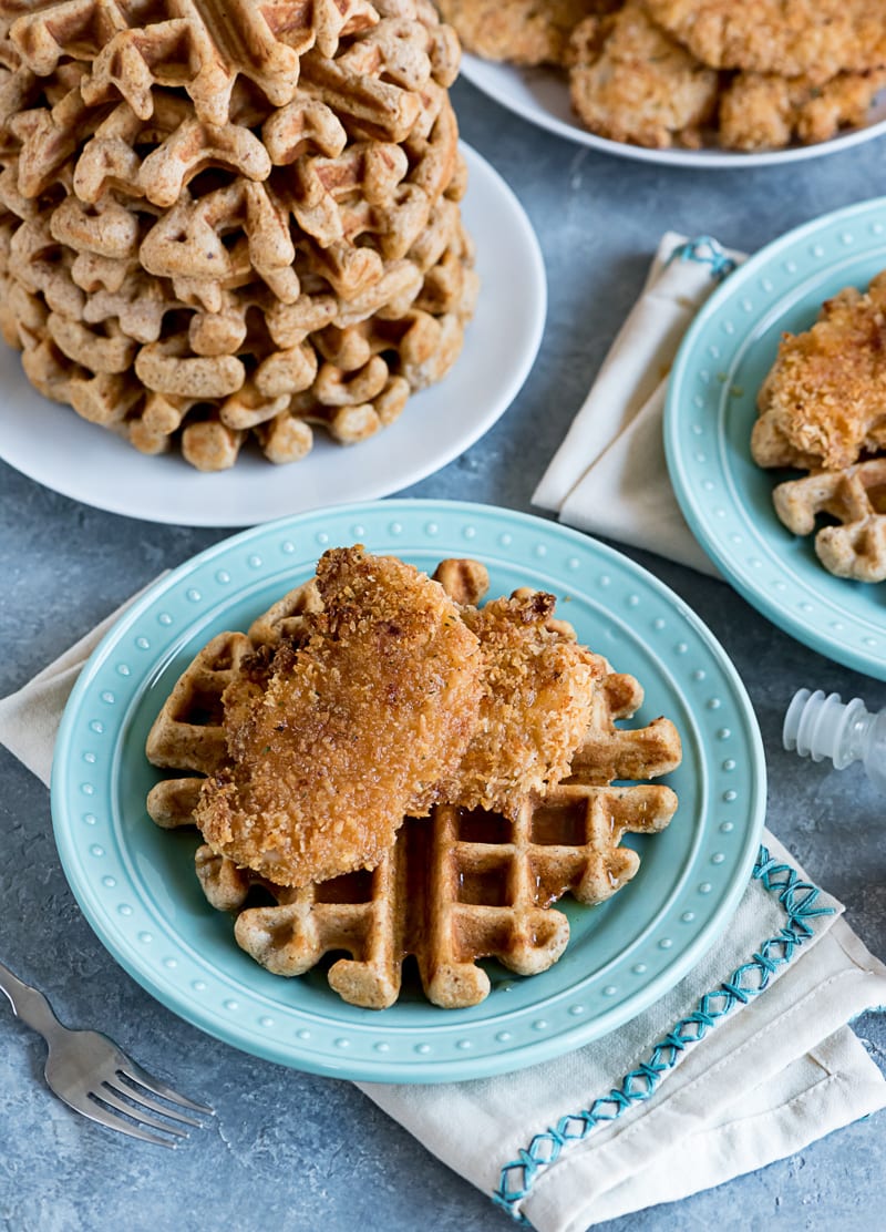 aqua plate with a waffle and two pieces of breaded baked chicken tenders, a plate with a stack of waffles