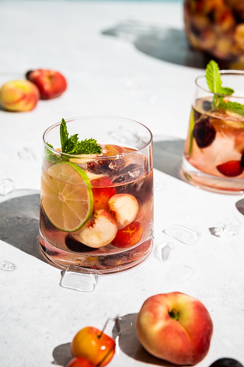 close up of glasses filled with ice, wine, fruit, cherries and peaches scattered on table