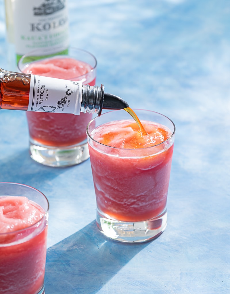 pink frozen rum runner cocktails in glasses, dark rum being poured over top of one of the cocktails