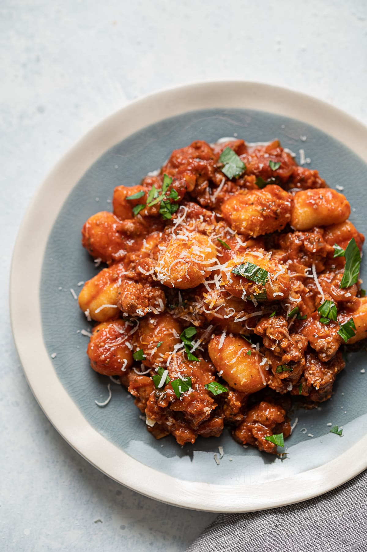 close up of small blue and white plate with red tomato sauce mixed with Italian sausage and gnocchi grated parmesan cheese and sliced fresh basil