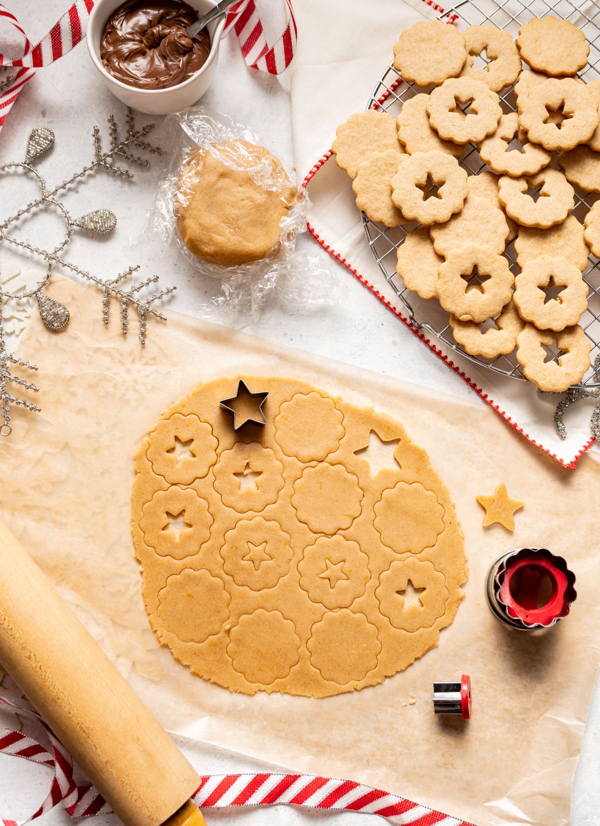 rolled out dough with cookie cut outs, wire rack with cookies cooling, dough rapped in plastic bowl of chocolate spread