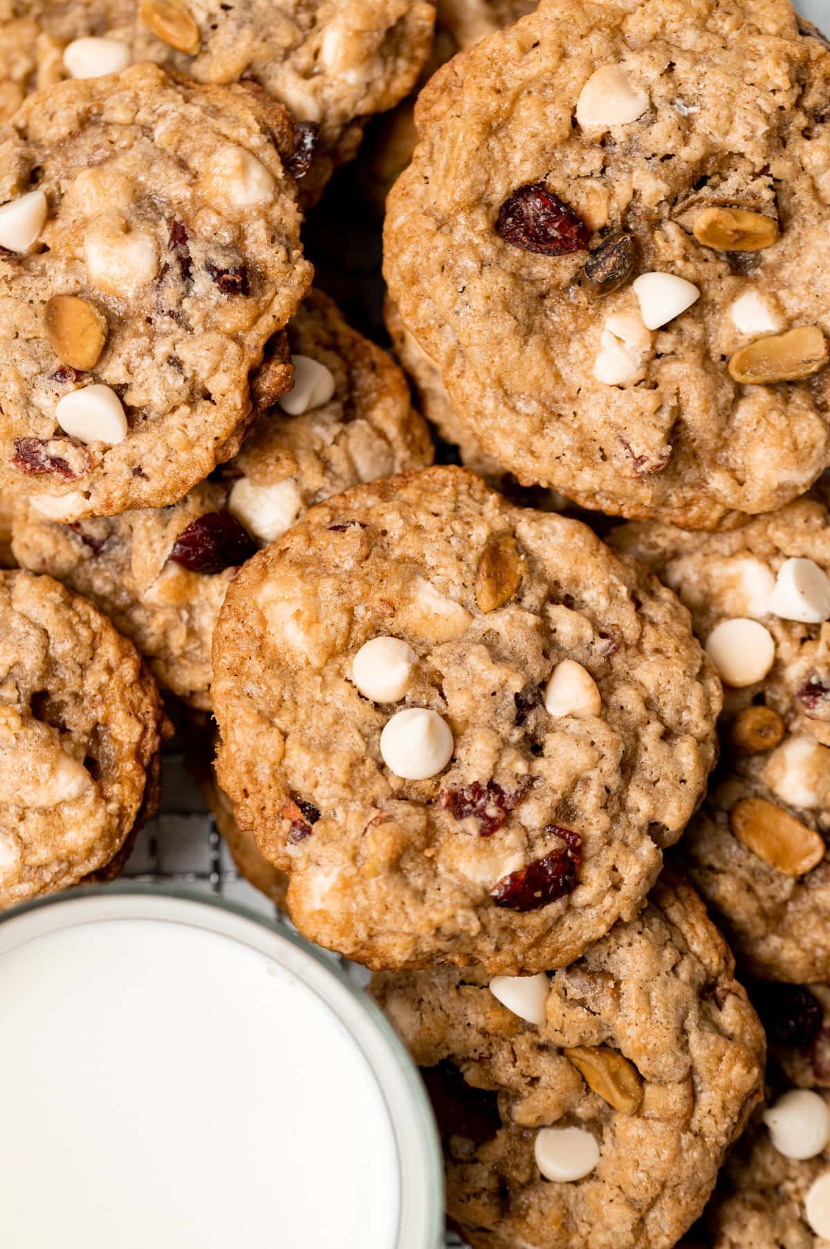 pile of oatmeal cookies with cranberries white chocolate chips and pistachios glass of milk