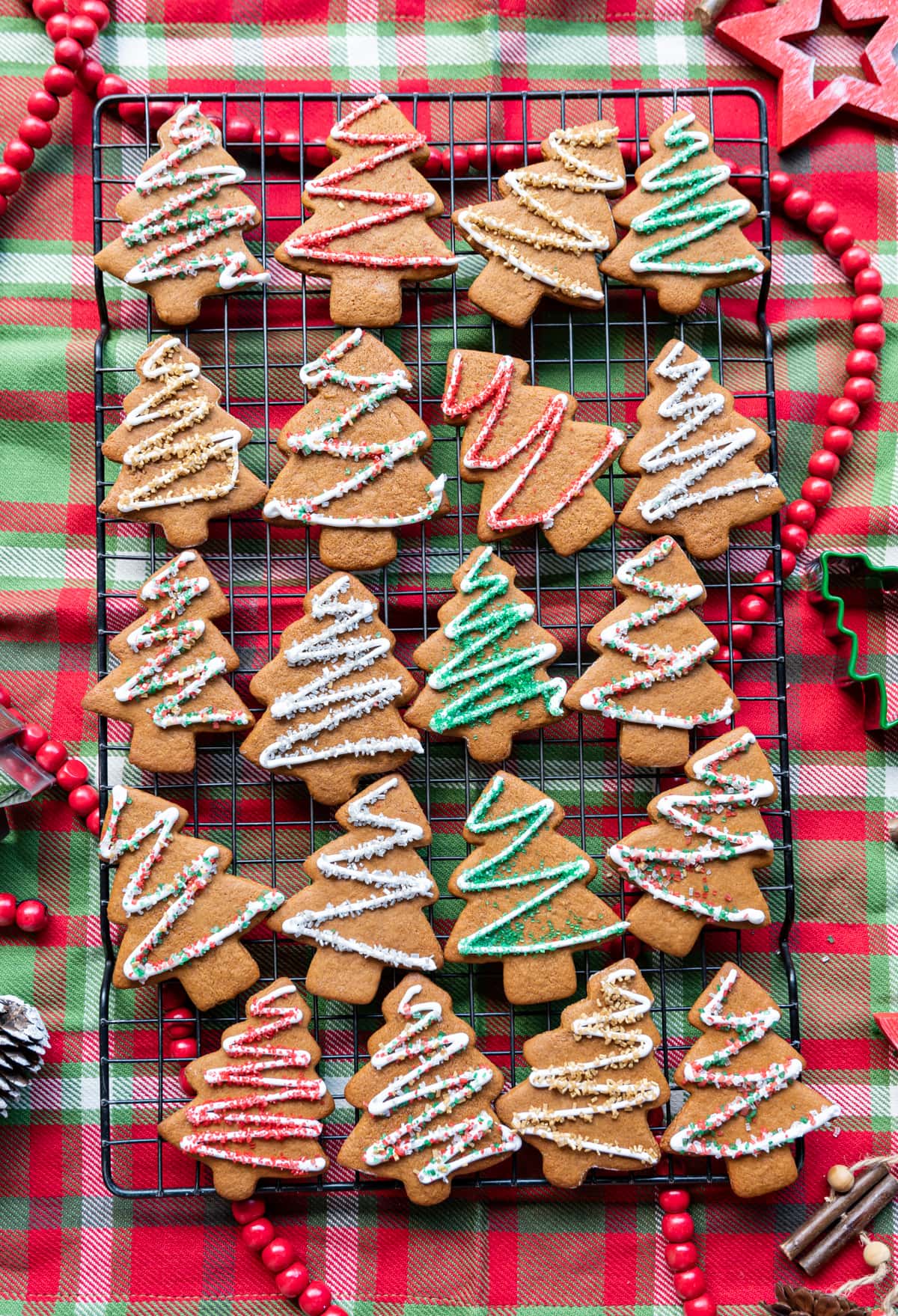 iced gingerbread christmas tree cookies on a wire rack on a red green and white plaid napkin
