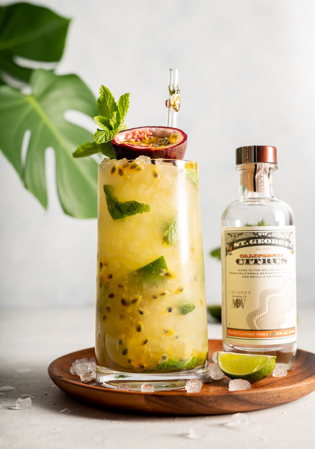 yellow cocktail with green mint and limes passion fruit and green monstera leaves bottle of vodka