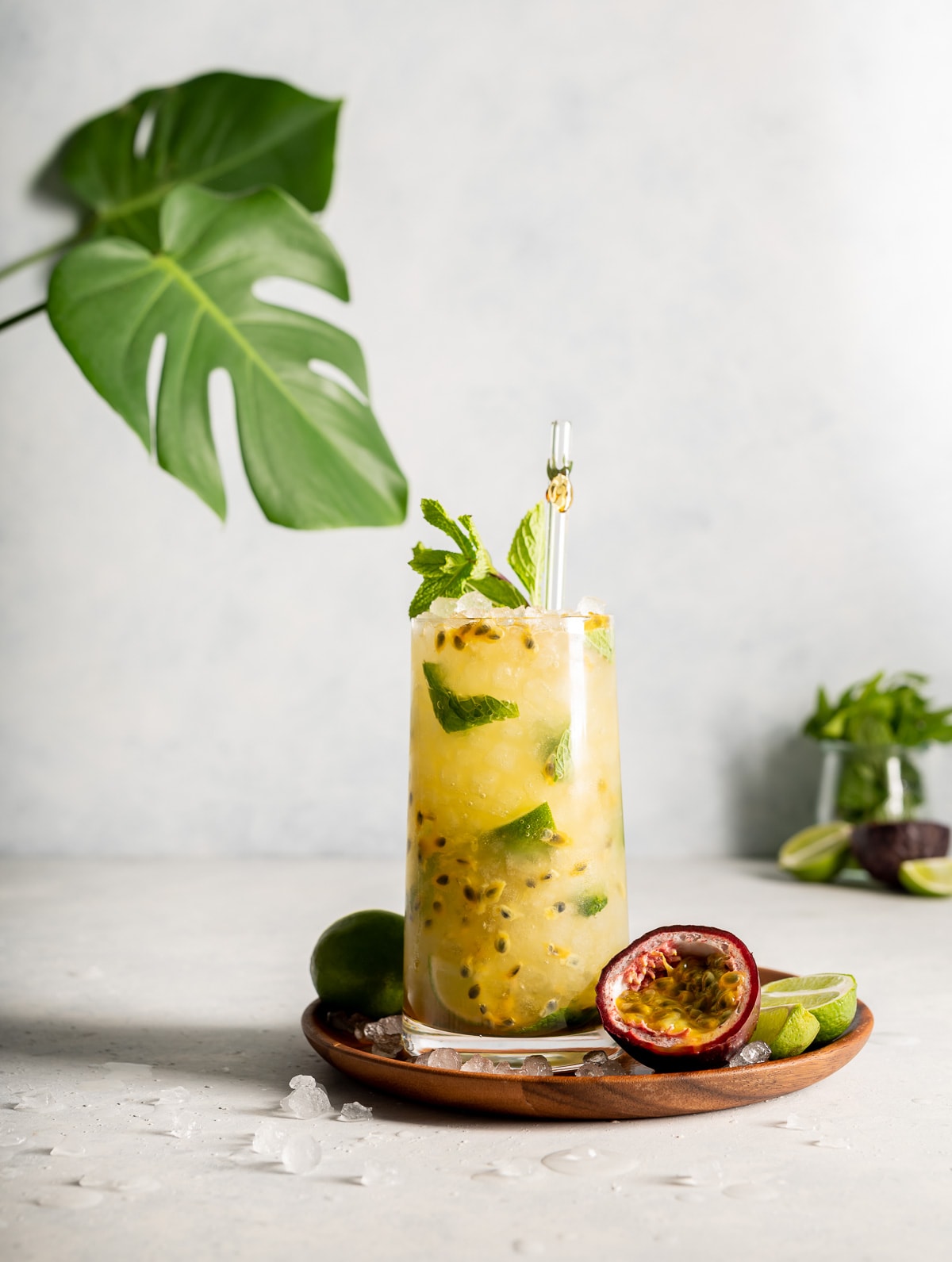 yellow cocktail with green limes, half a passion fruit, monstera leaves