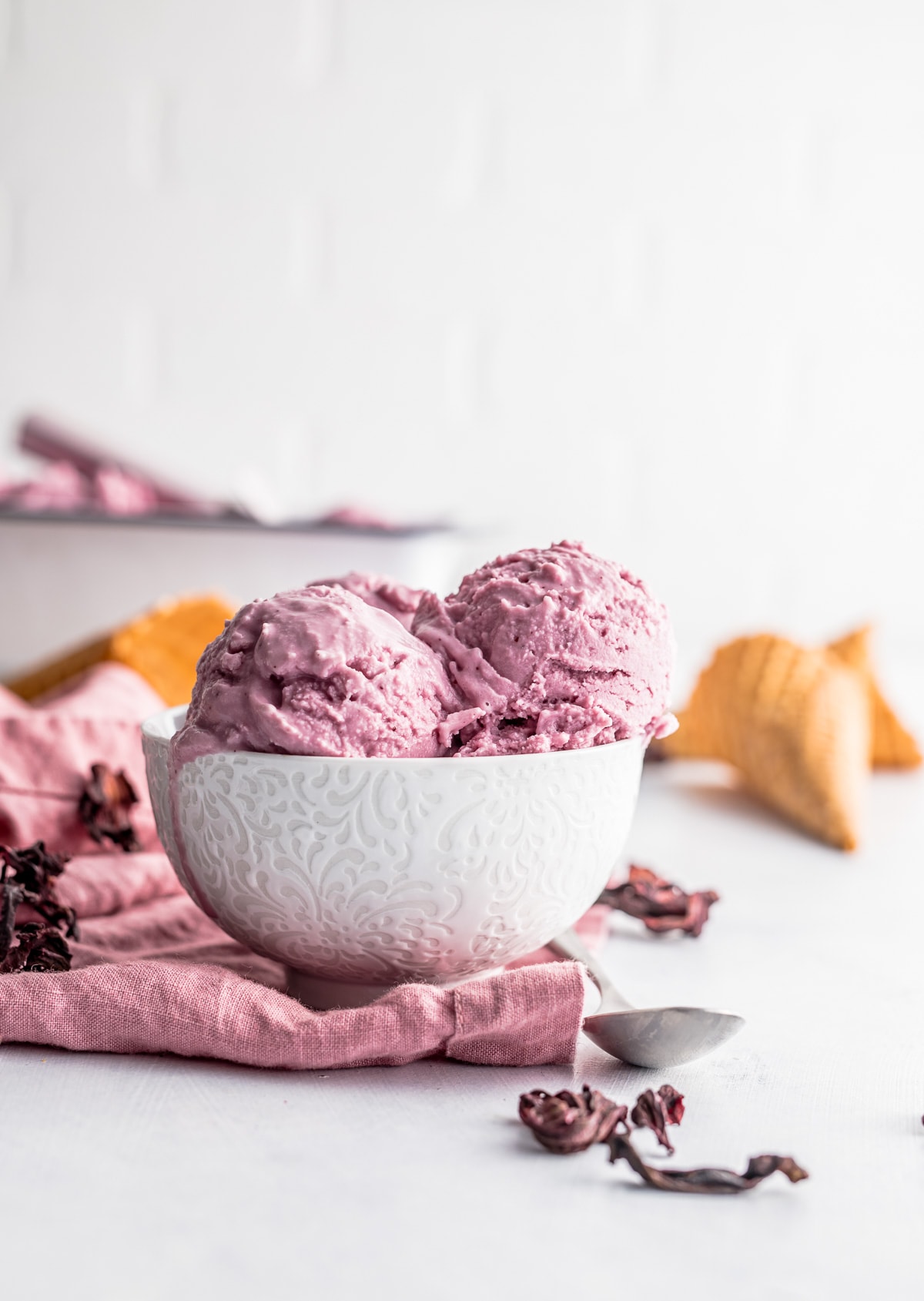 scoops of pink ice cream in a white bowl on a pink napkin scattered hibiscus flowers