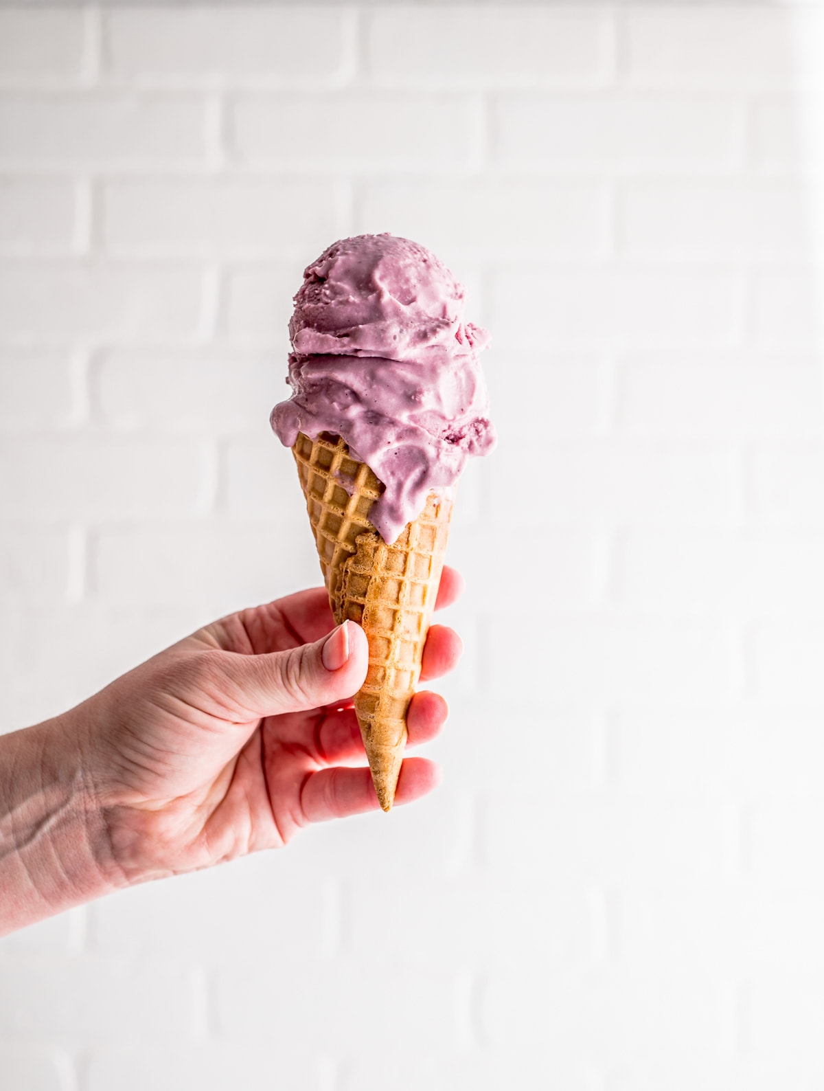 hand holding up a waffle ice cream cone with two scoops of pink ice cream