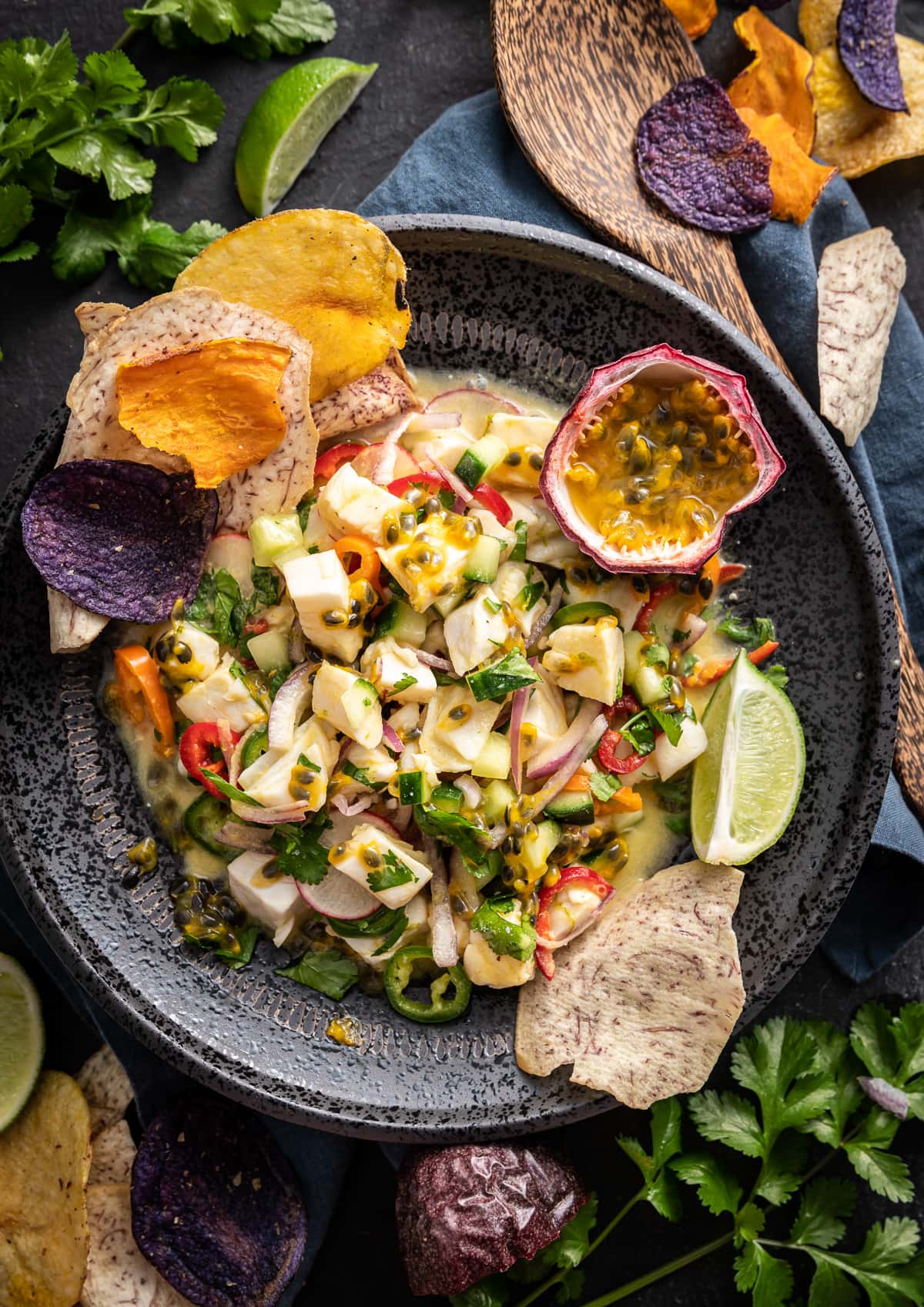 halibut passion fruit ceviche in a black bowl with fresh passion fruit and vegetable chips