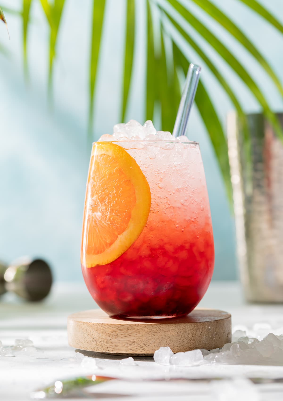 hibiscus spritz red and white cocktail with orange slice yellow plumeria palm leaves