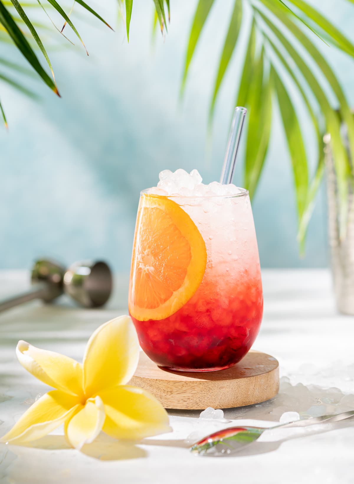 red and white cocktail with orange slice yellow plumeria palm leaves