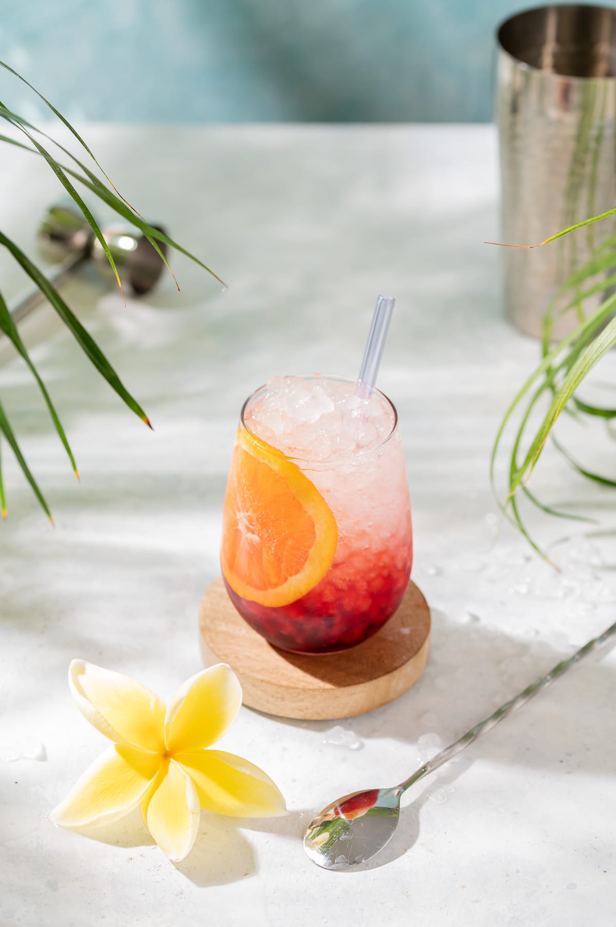 red and white cocktail with orange slice yellow plumeria palm leaves