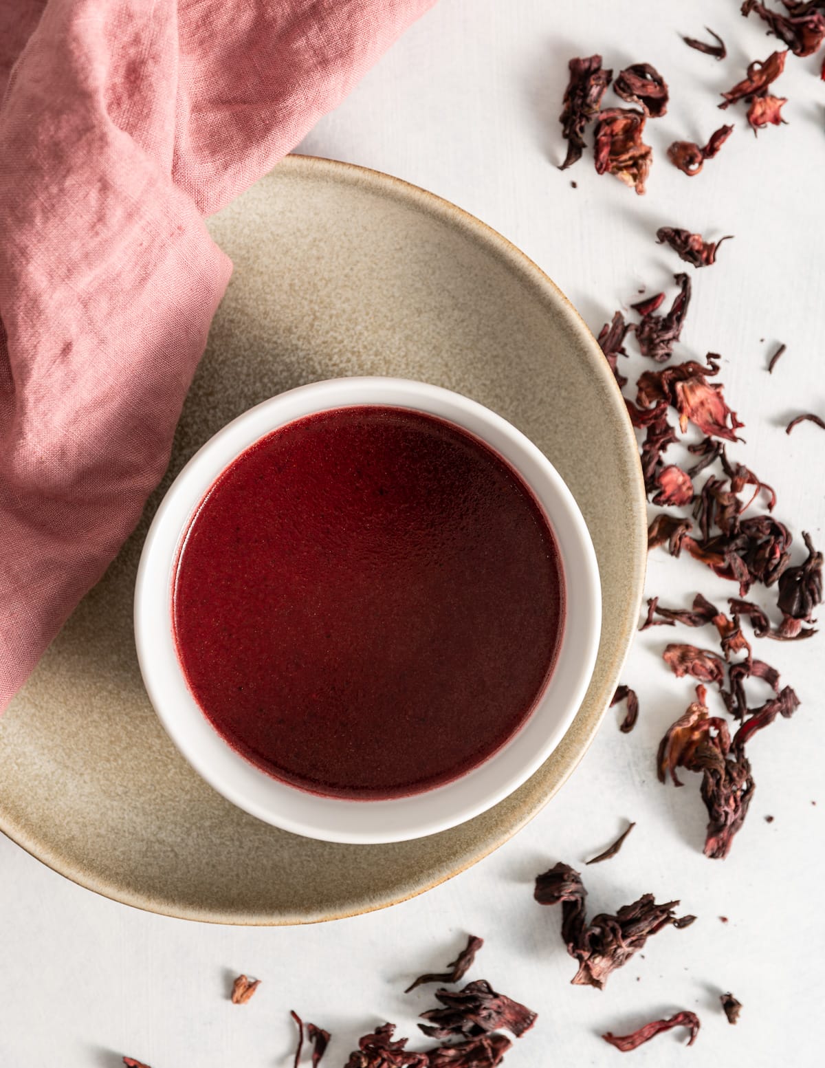 dark red version of hibiscus vinaigrette in a white bowl on a tan plate 