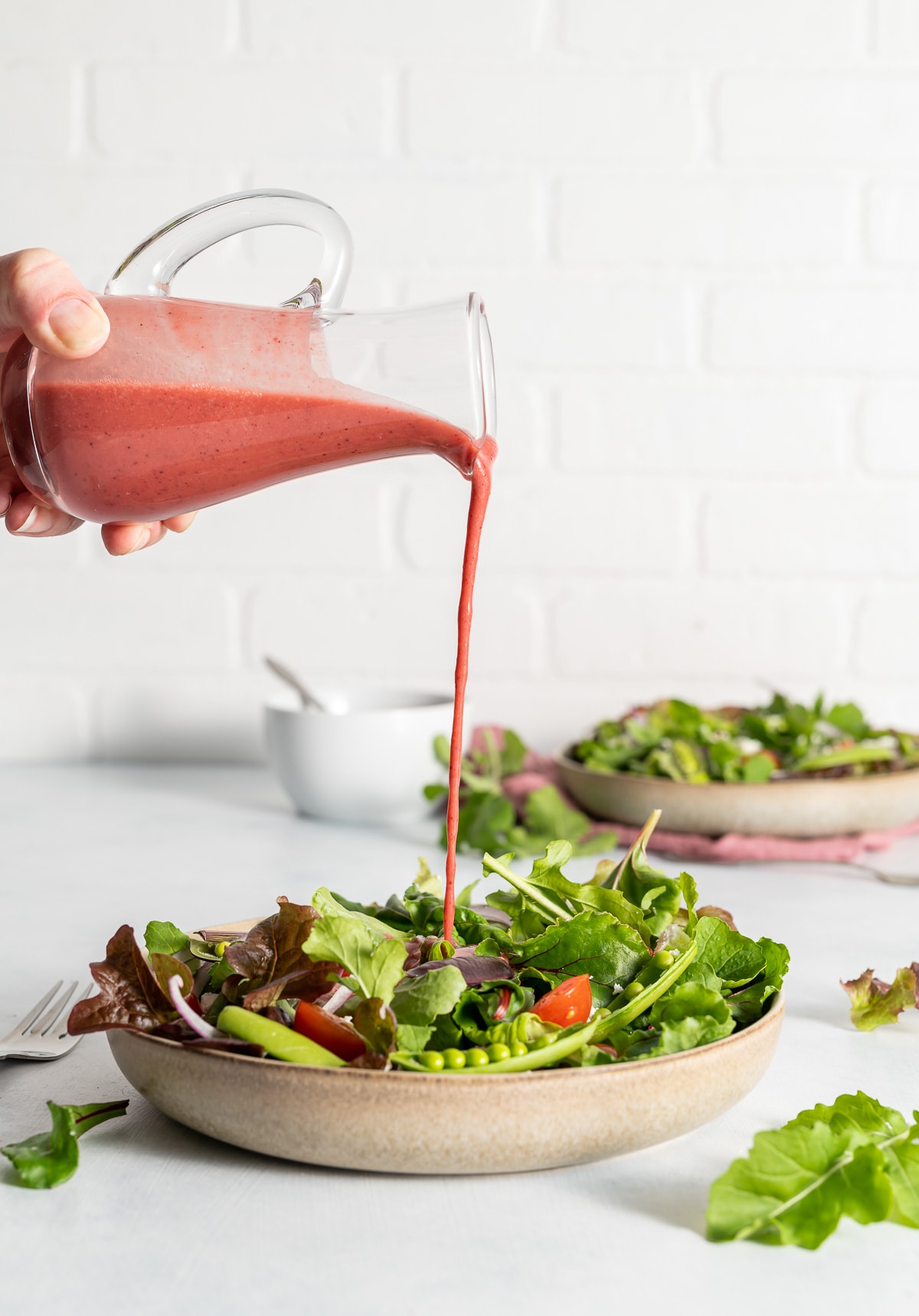 pink hibiscus vinaigrette dressing being poured onto a bowl of salad greens