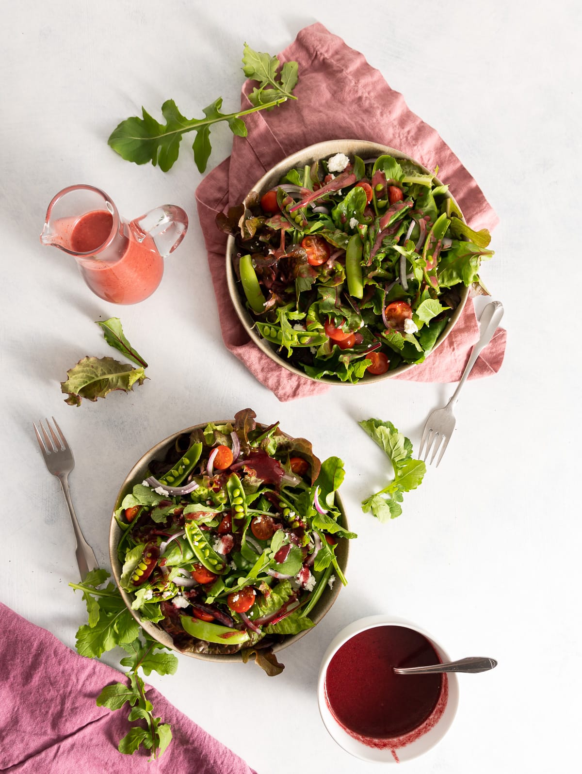two bowls of salad greens with pink and dark red vinaigrette dressings 