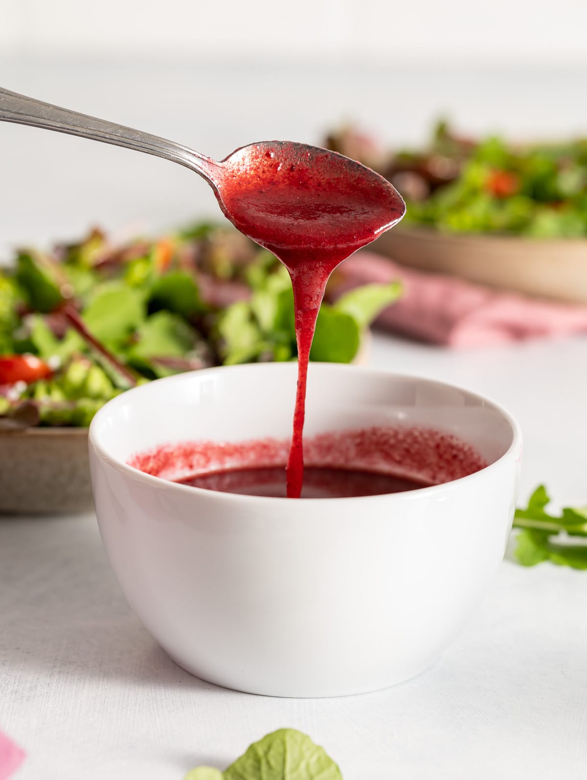 spoonful of dark red vinaigrette dressing being poured into a white bowl