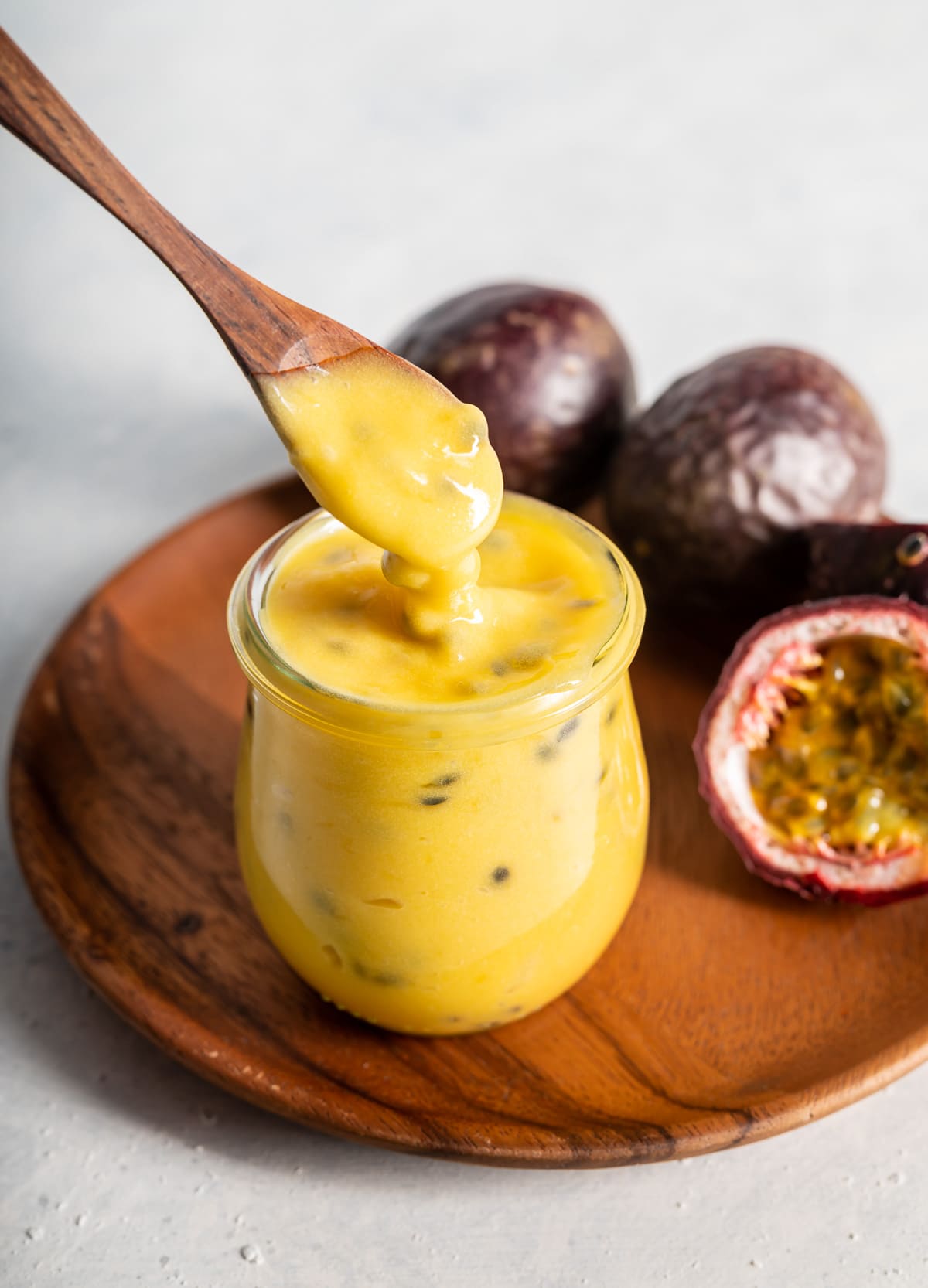 brown spoon with yellow passion fruit curd in a jar with fresh passion fruits cut in half brown plate