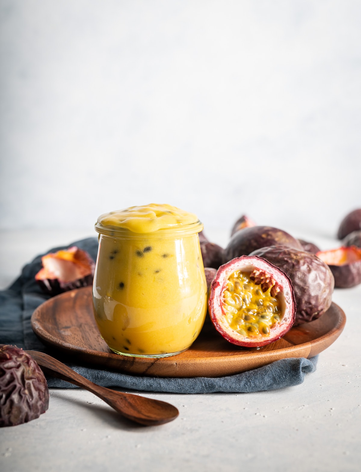 yellow passion fruit curd in a jar with fresh passion fruits cut in half brown plate blue napkin