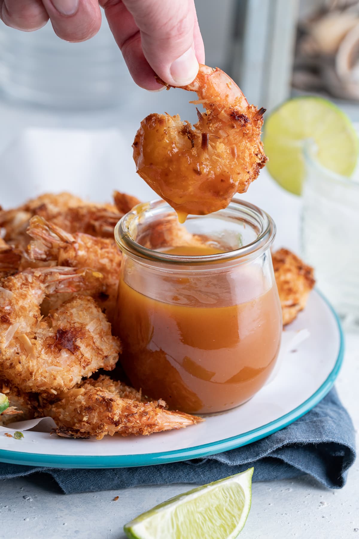 coconut shrimp being dipped into a jar of habanero passion fruit dipping sauce