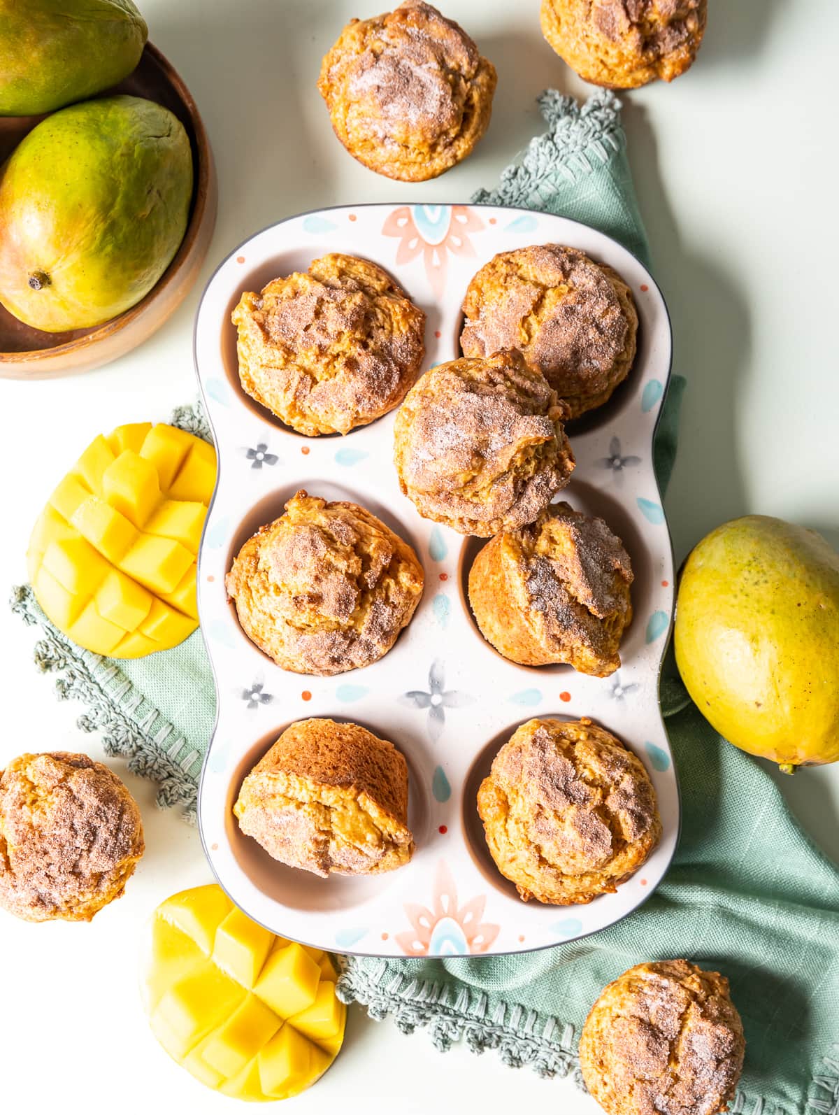 tropical cinnamon mango muffins in a ceramic muffin tin with whole and cut mangoes