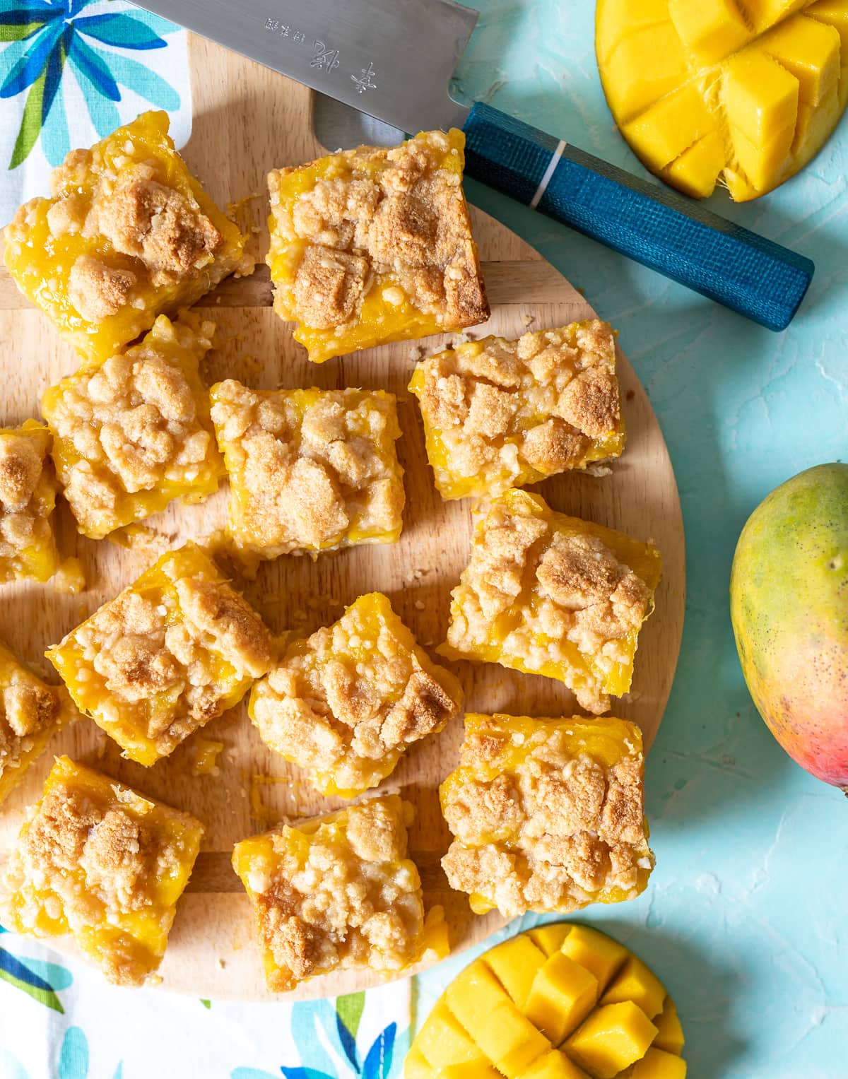 malted macadamia mango crumb bars cut into squares on a cutting board, knife with blue handle cut mangoes