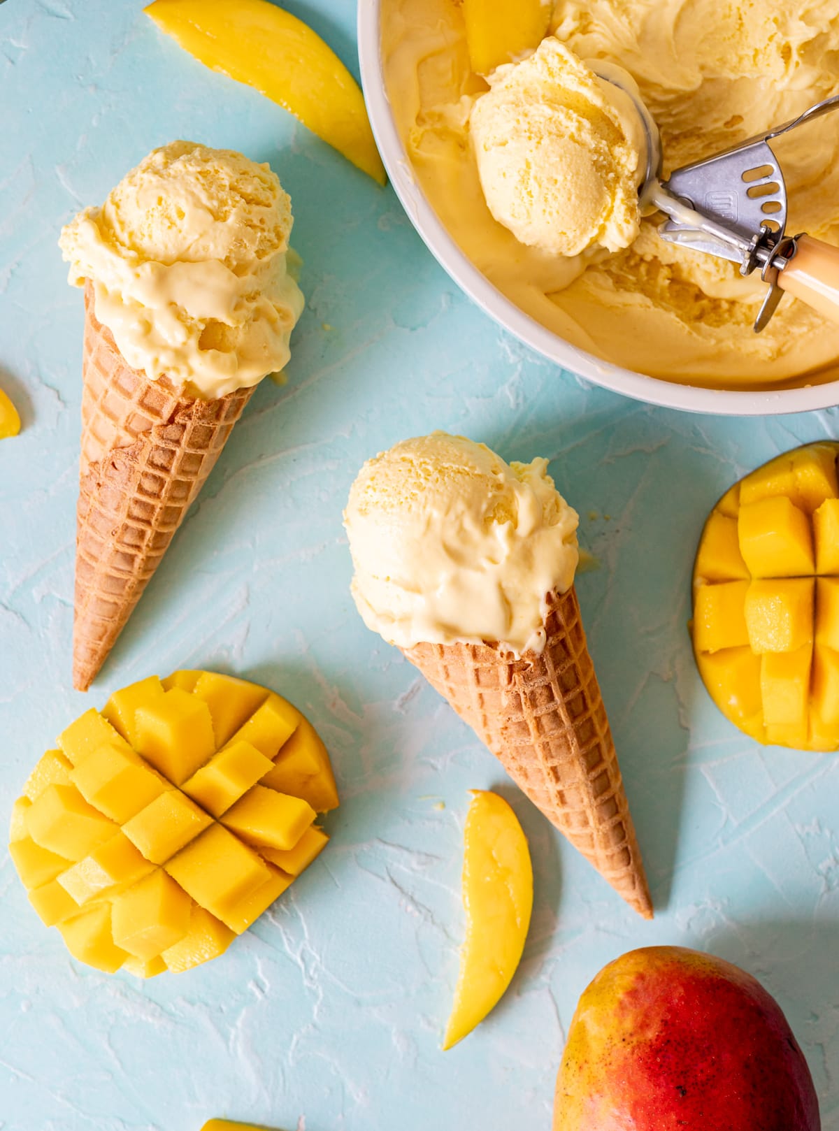 yellow mango ice cream in cones cut mango halves mango ice cream in scoop in bowl