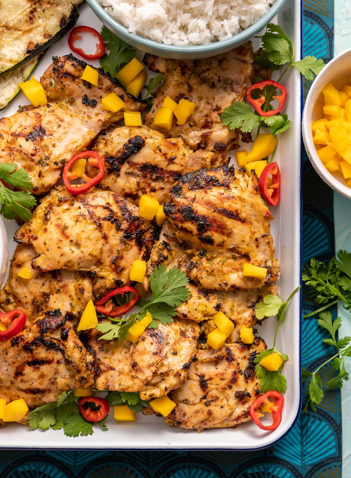 grilled chicken on a tray with mango and red chili slices cilanto pieces