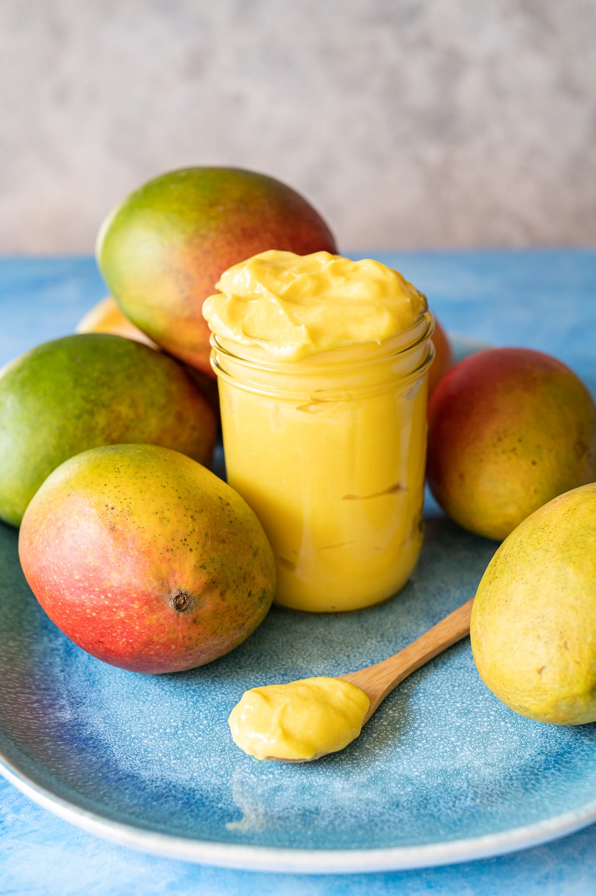 yellow mango curd in a jar on a blue plate with whole mangoes