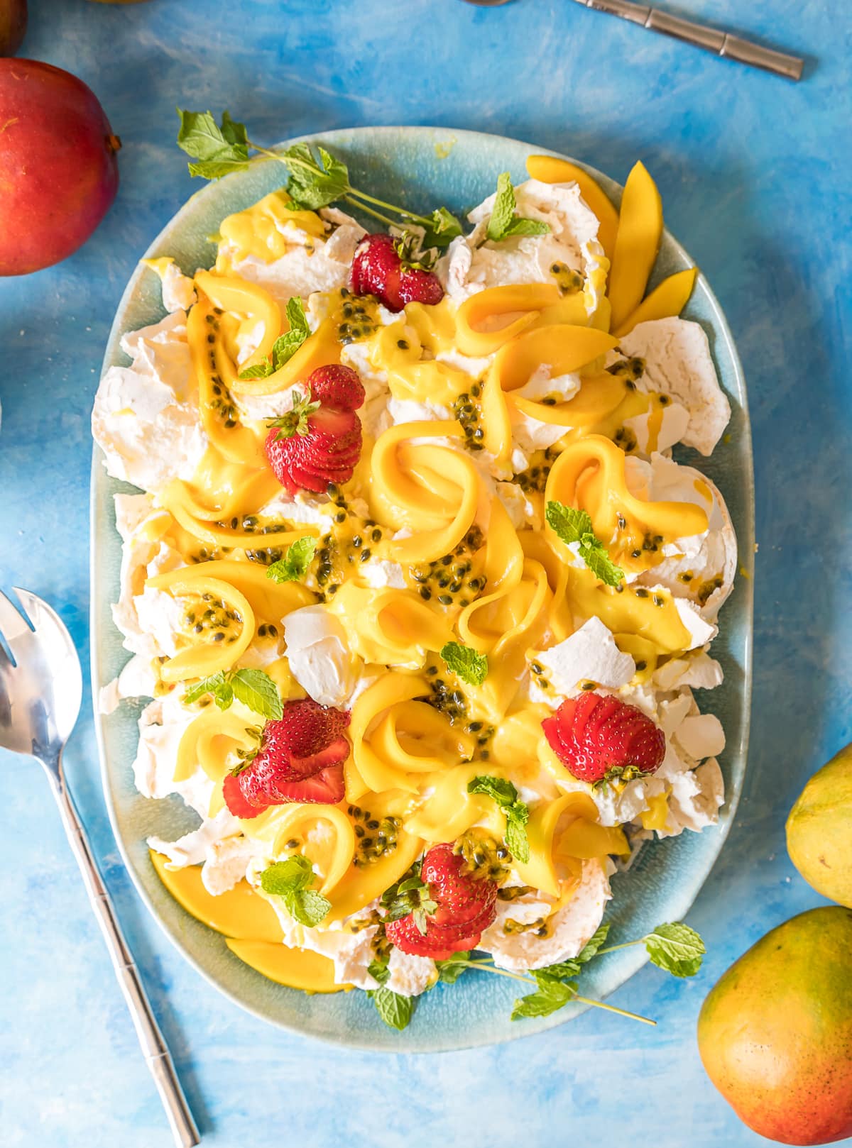 smashed pavlova on a blue platter with mangoes passion fruit and strawberries