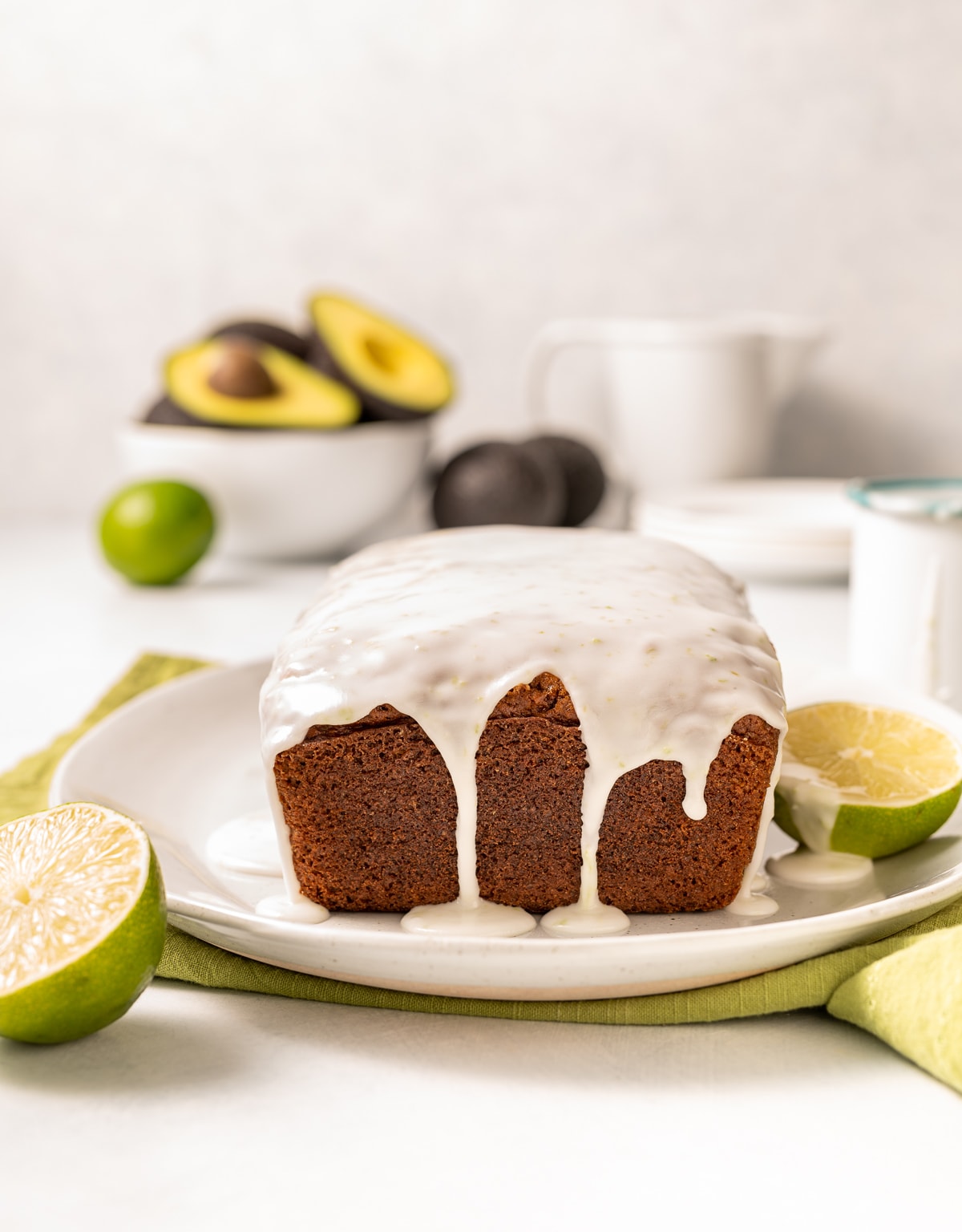 whole loaf of lime glazed avocado bread with lime slices and bowl of avocados