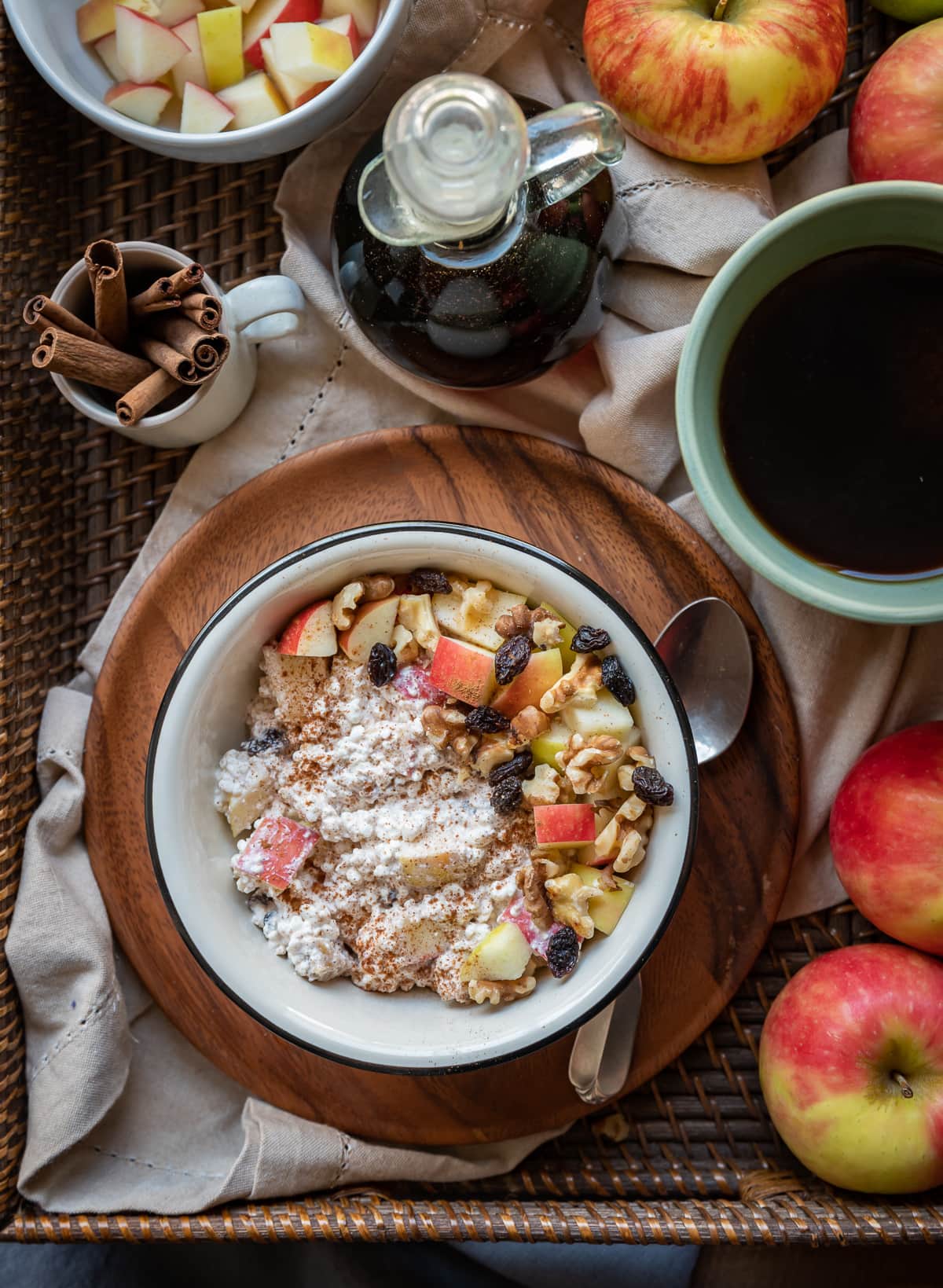 brown basket with apples cup of tea cup with cinnamon sticks cinnamon white bowl on brown plate filled with apple cottage cheese breakfast bowl