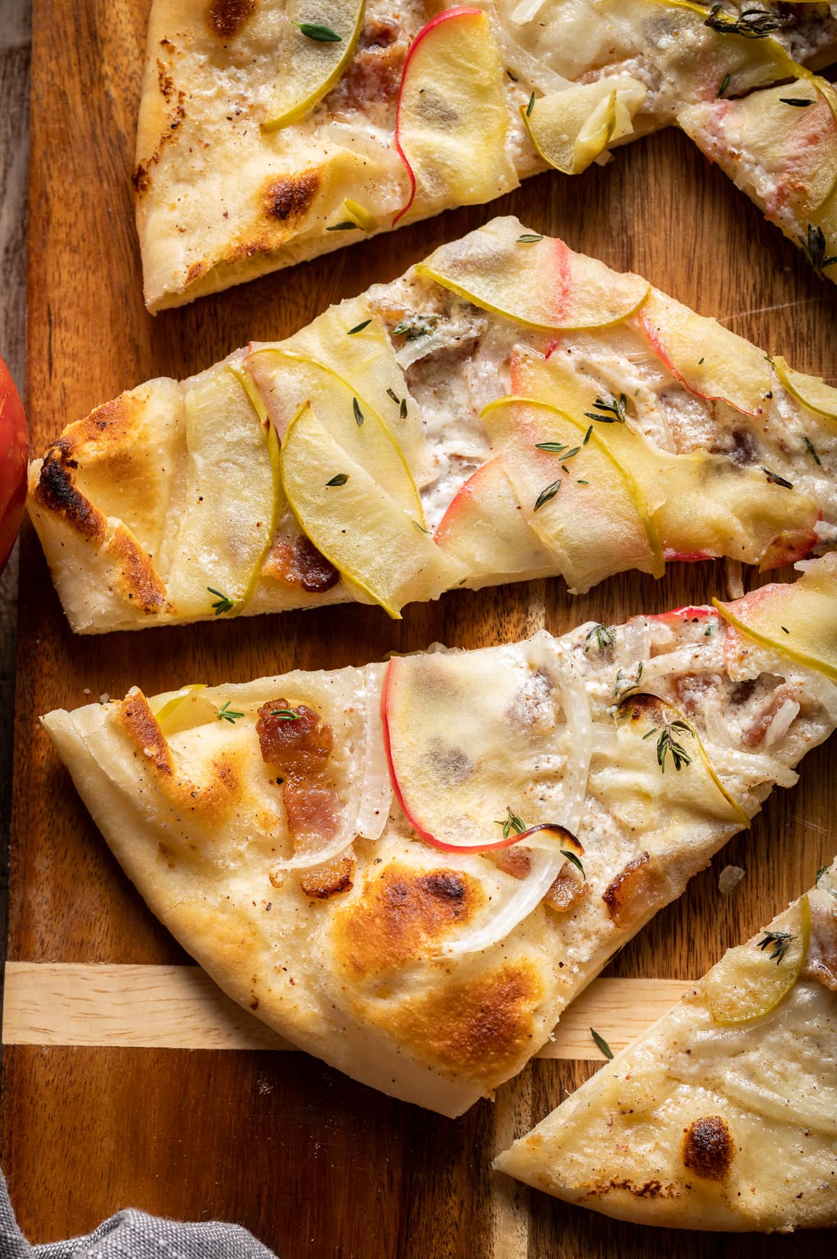 slices of flammkuchen on a cutting board with apples onions bacon and thyme