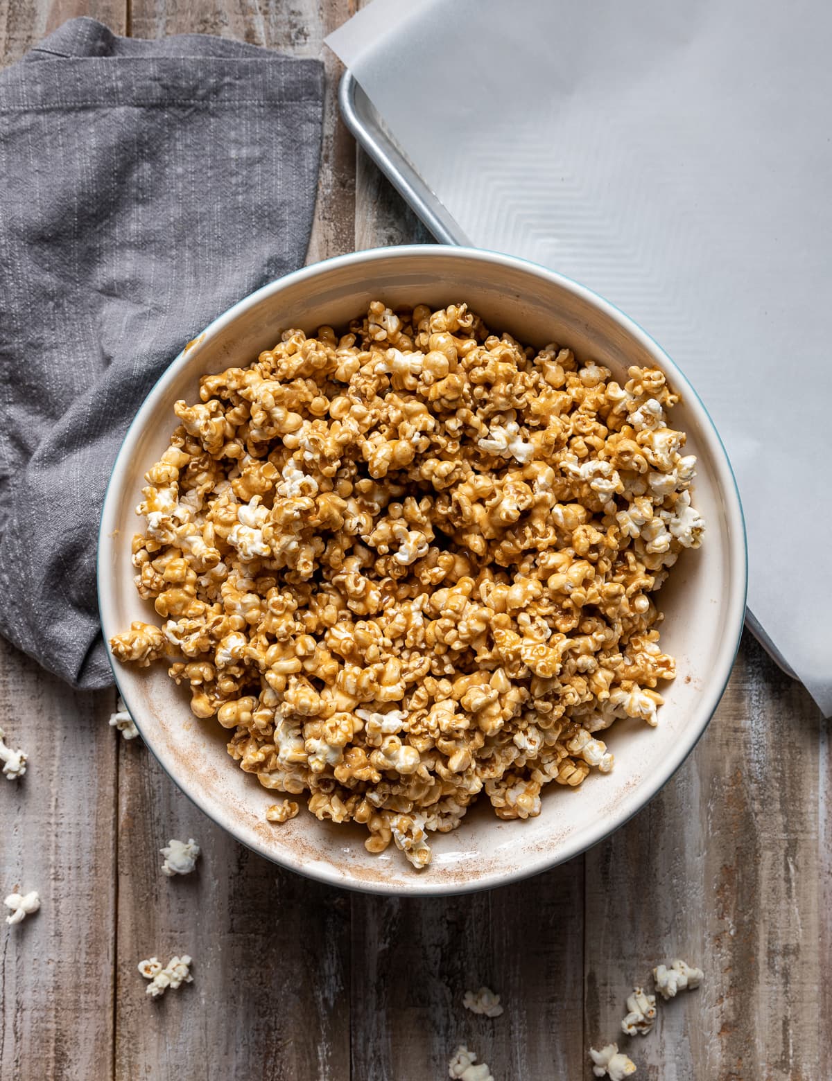 large white bowl of popped popcorn covered with brown caramel sauce gray napkin white paper lined baking tray