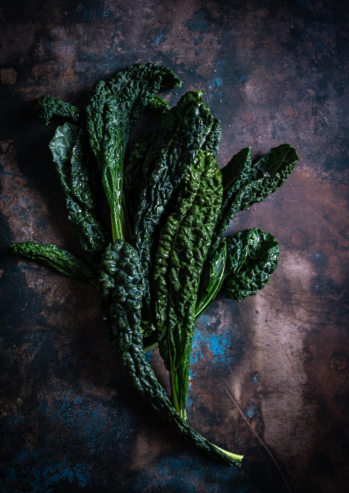 bunch of dark green tuscan kale leaves on a brown and blue surface